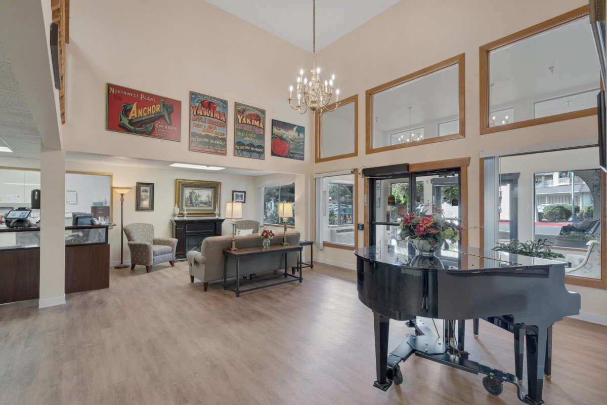 A spacious living room featuring a grand piano, chandelier, and decorative artwork.