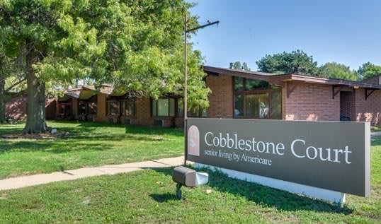 Entrance to Cobblestone Crossing community building with a prominent sign and surrounding greenery.
