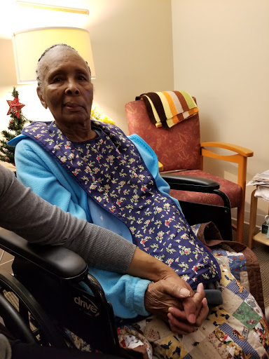 An elderly woman in a wheelchair being comforted by another person.
