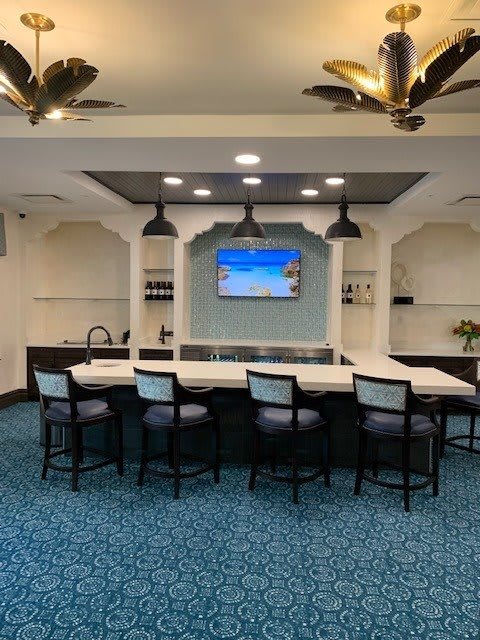 A modern lounge area featuring a bar counter with seating, pendant lighting, and a television.