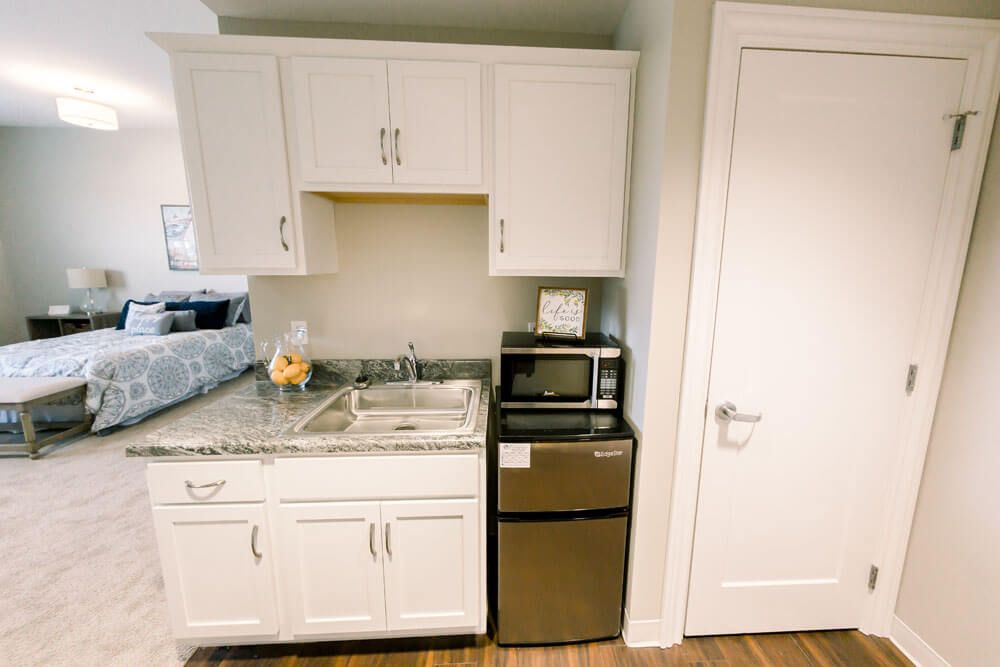 A compact kitchen area with white cabinets, a sink, a microwave, and a mini fridge.