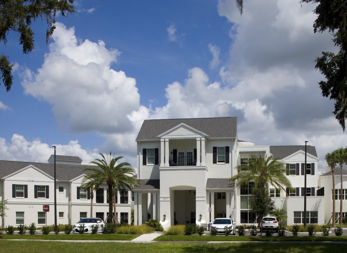 A modern apartment building surrounded by palm trees under a partly cloudy sky.