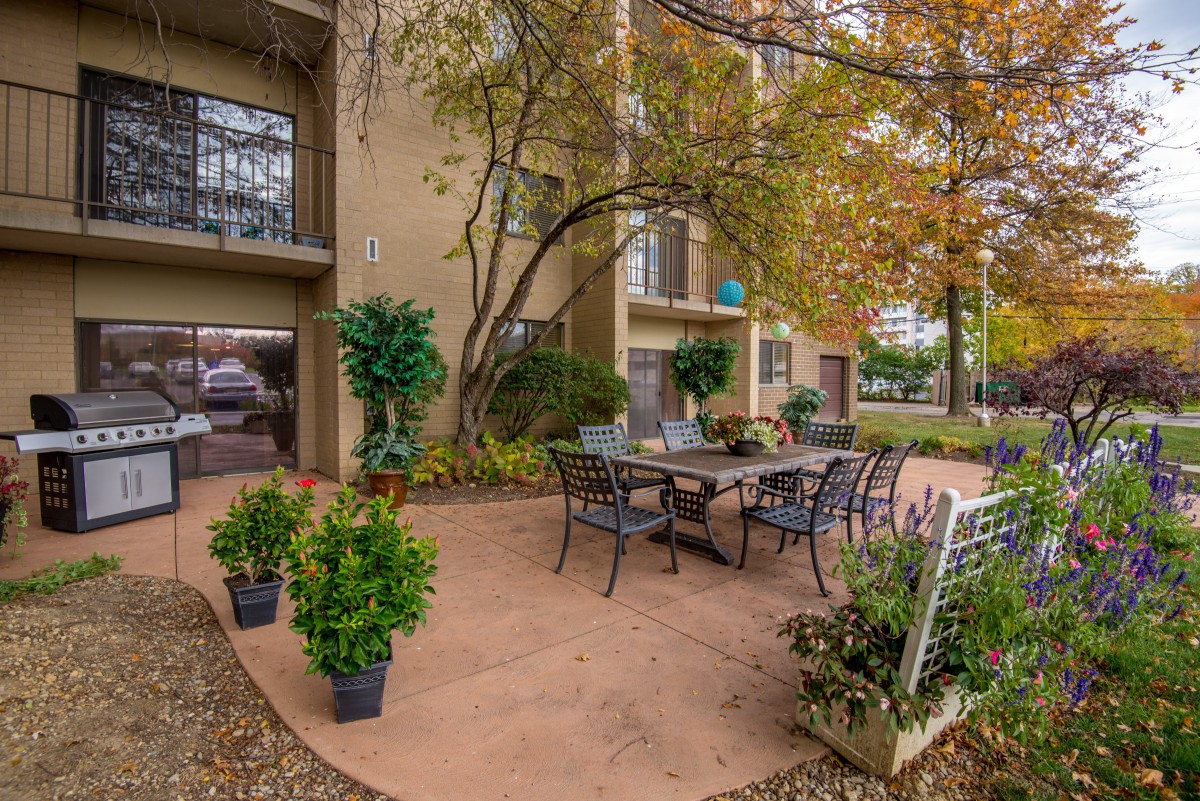 A welcoming outdoor patio area at an apartment complex, featuring a table and chairs surrounded by lush greenery.