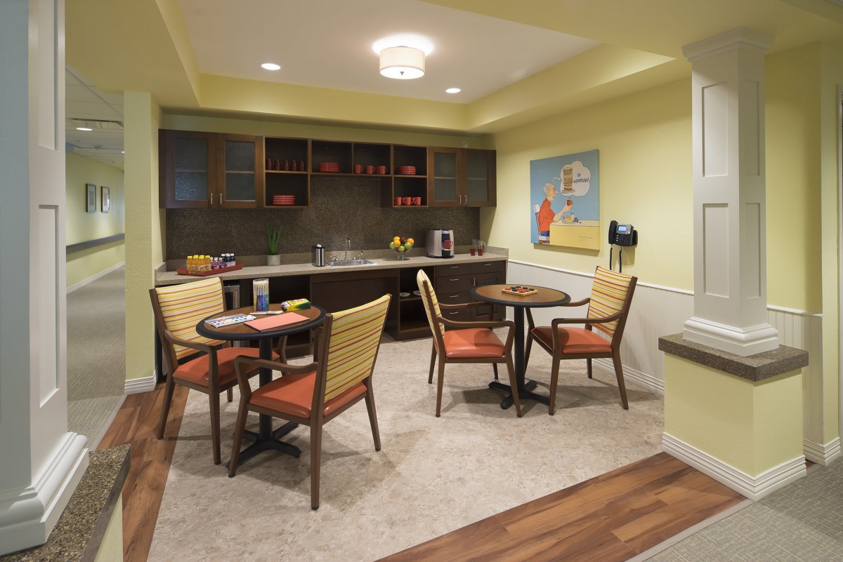 A cozy dining area with a small kitchen space, featuring tables and chairs, warm lighting, and modern decor.