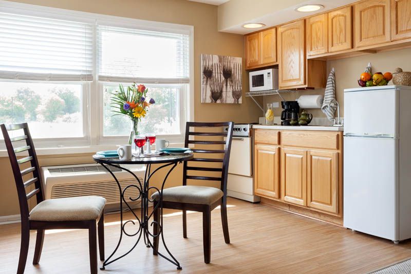 A cozy kitchen with a small dining table and chairs, featuring light wooden cabinets and a large window.