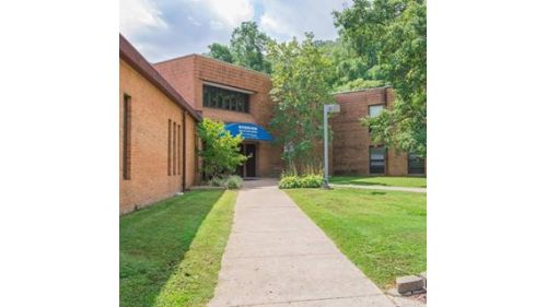 A welcoming entrance to a brick school building surrounded by lush greenery.