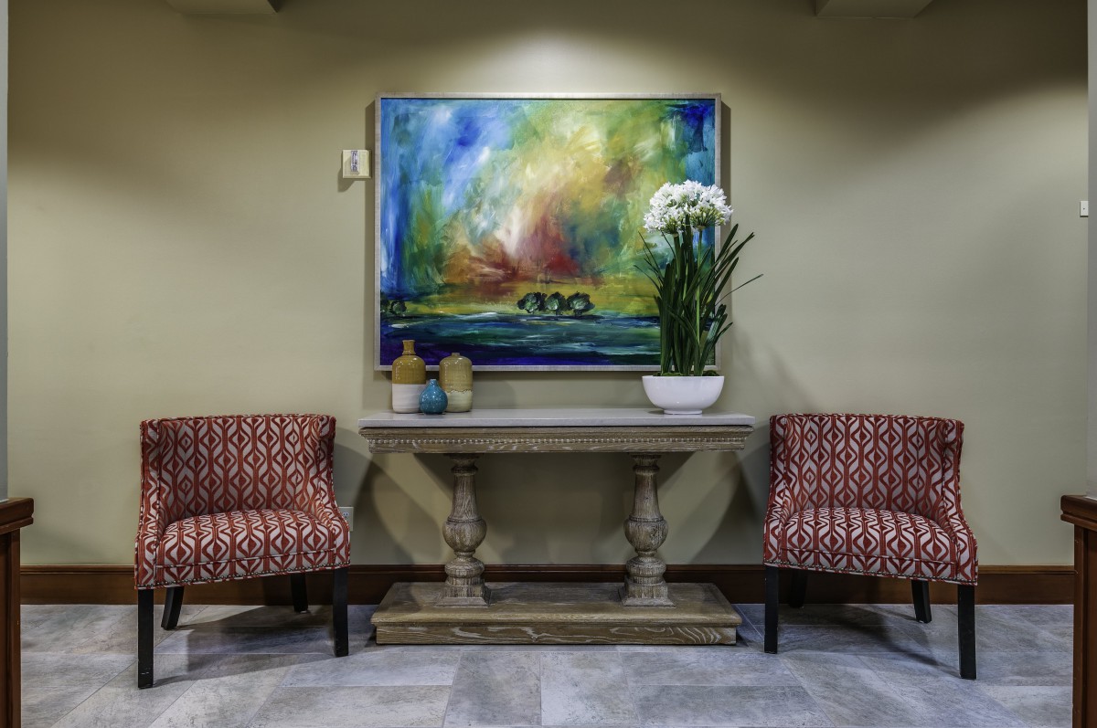 A cozy interior with two patterned chairs, a wooden table adorned with flowers, and a vibrant abstract painting on the wall.