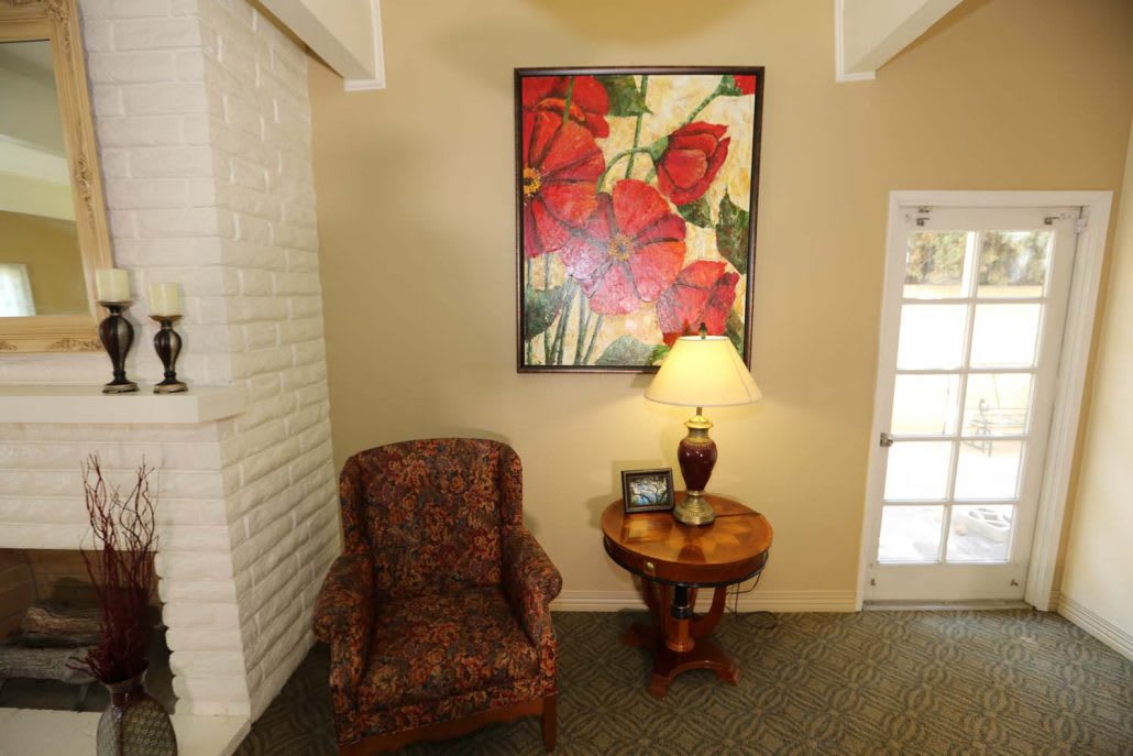 A cozy living room corner featuring a patterned armchair, side table with a lamp, and a vibrant floral painting on the wall.