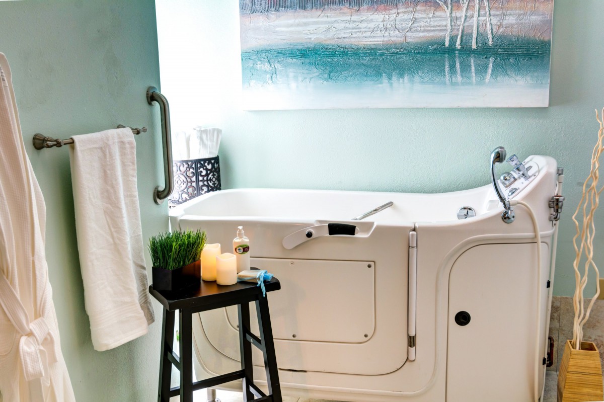 A modern bathroom featuring a walk-in tub with accessibility features, decorated with candles and a towel.