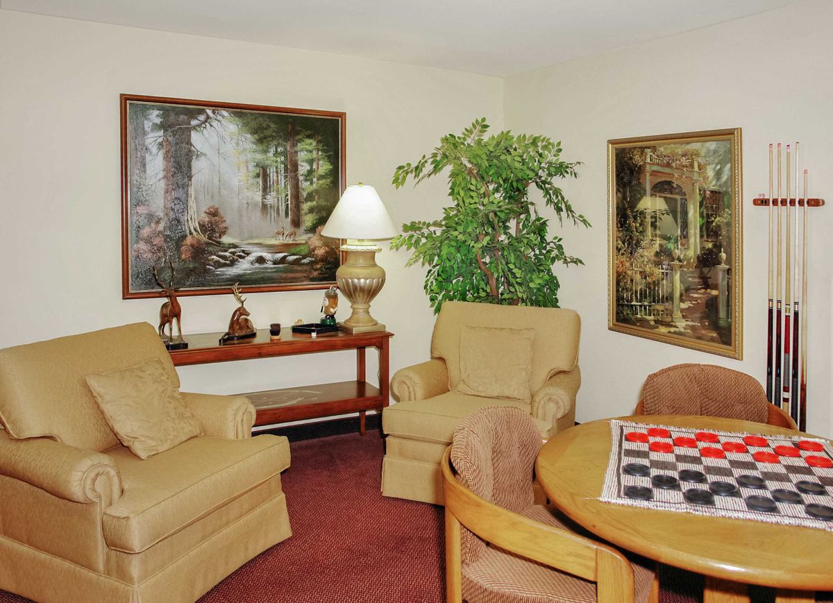 A cozy living room with comfortable chairs, a table with a checkerboard, and decorative artwork on the walls.