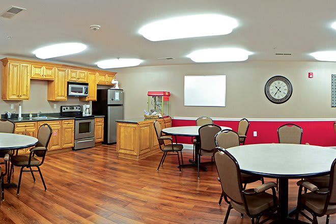 A kitchen and dining area with wooden cabinets, round tables, and chairs on a hardwood floor.