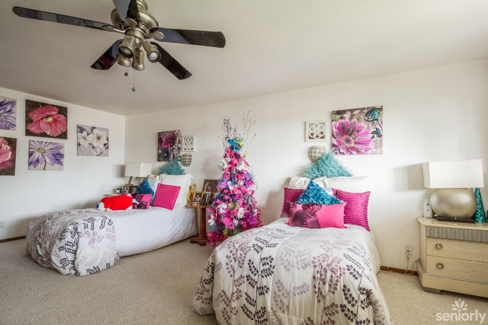 A cozy bedroom with twin beds adorned with pink and floral decor, featuring a ceiling fan.