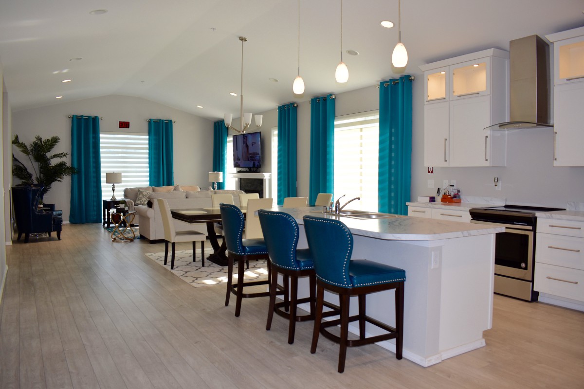 A modern open-plan kitchen and dining area featuring blue bar stools, pendant lighting, and large windows with blue curtains.