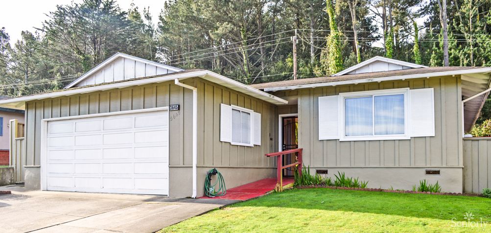 A single-story house with a garage and front yard, surrounded by trees.