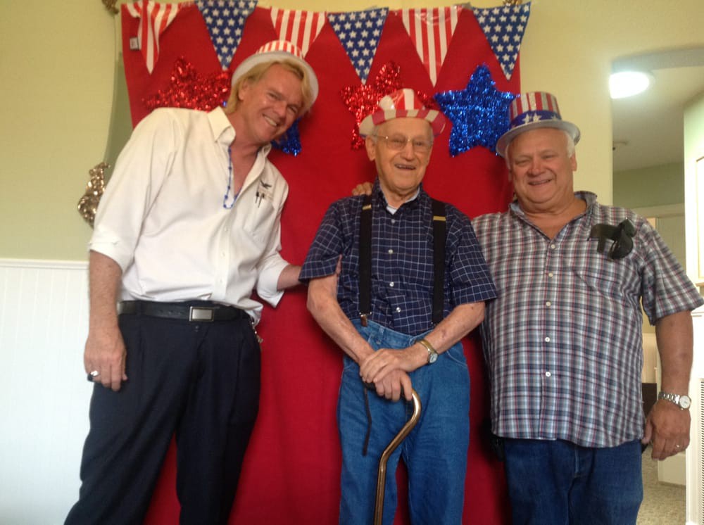 Three men in festive attire pose in front of a patriotic backdrop.