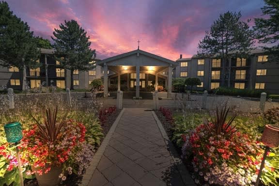 A beautifully lit building at sunset, framed by vibrant gardens and a welcoming pathway.