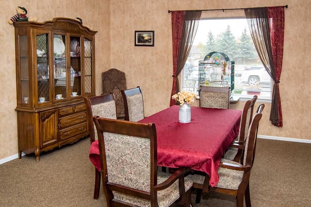 A cozy dining room with a red tablecloth on the table, surrounded by wooden chairs and a china cabinet.