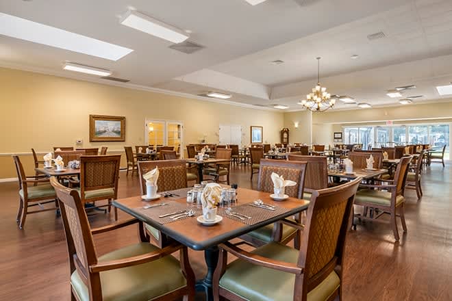 An elegant dining room with neatly arranged tables and chairs under a chandelier.