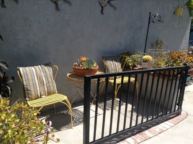 A sunny patio with two chairs and a table surrounded by plants.