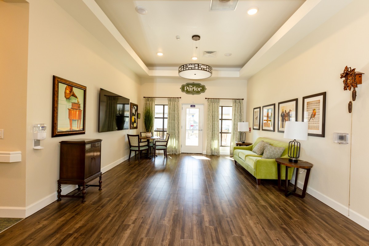 A modern living room with a hardwood floor, featuring a green sofa, artwork on the walls, and ample natural lighting.