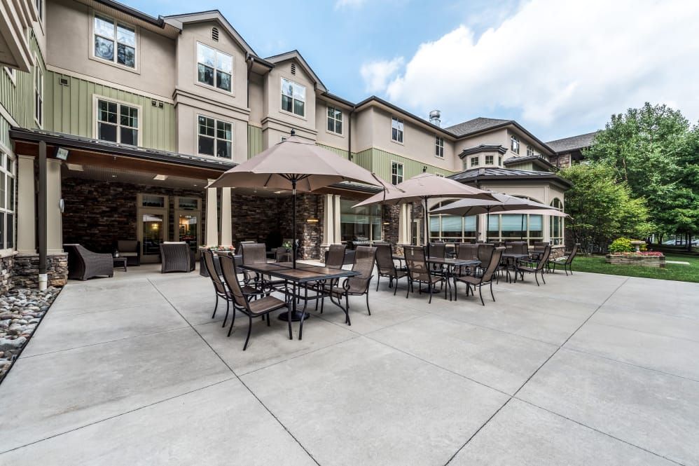An outdoor patio area with tables, chairs, and umbrellas in front of a residential building.