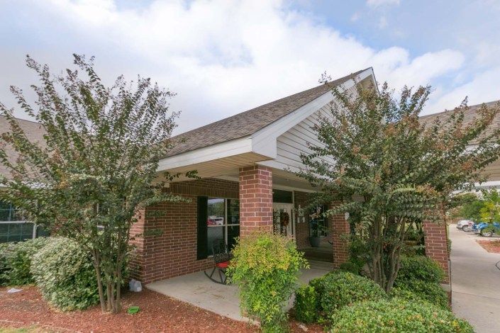A cozy brick house with a covered porch, surrounded by shrubs and trees.