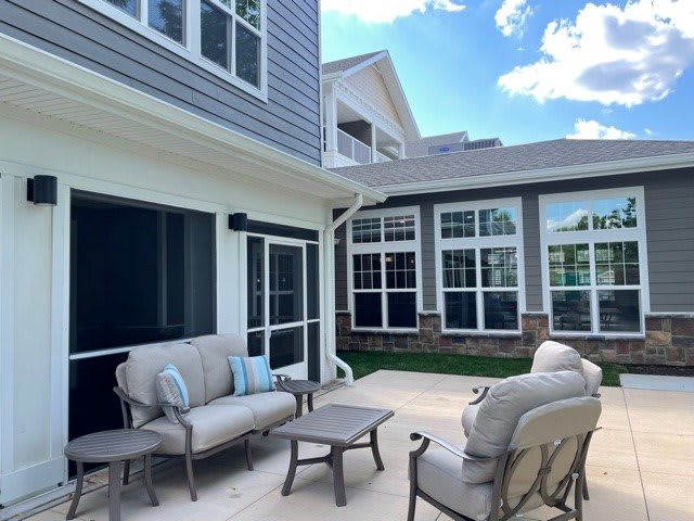 A cozy outdoor patio area with comfortable seating and a small table, set against the backdrop of a modern house on a sunny day.