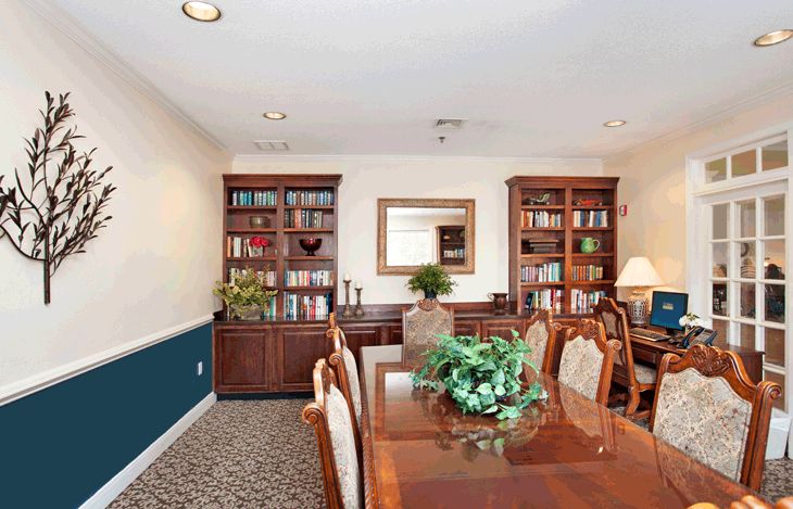 A well-furnished conference room featuring wooden bookshelves, a large meeting table, and elegant chairs with decorative plants on display.