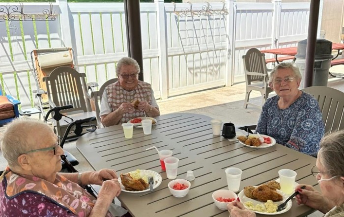 A group of elderly individuals enjoying a meal together outdoors on a sunny day.