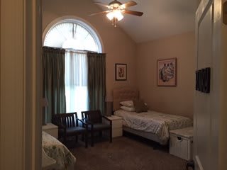 A cozy bedroom with a single bed, chairs, and a large window with curtains.