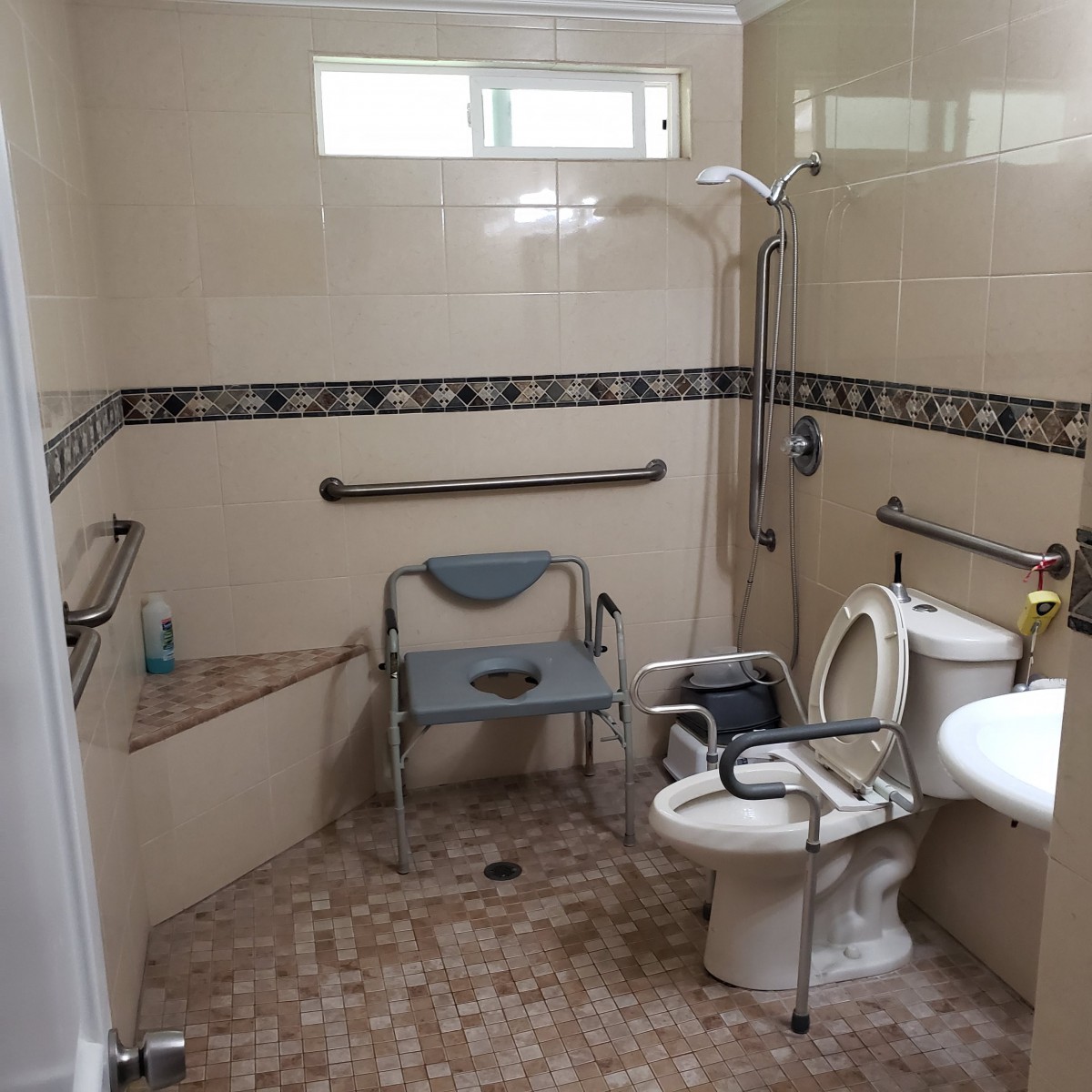 An accessible bathroom equipped with a toilet, shower, grab bars, and a corner seat.