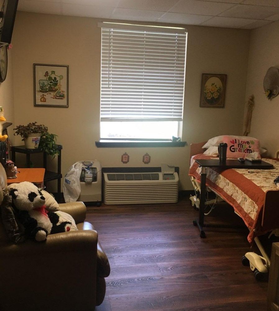 A cozy bedroom with simple decor, featuring a bed, stuffed animal, and seating area.