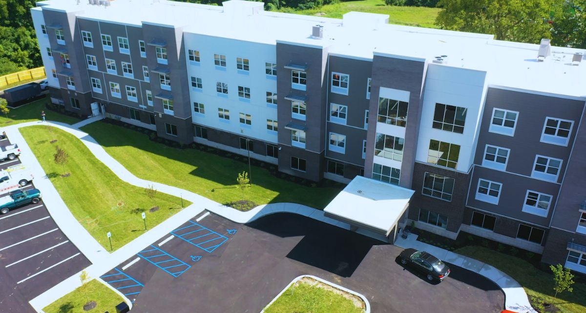 A modern residential apartment building with a neatly landscaped parking area, viewed from above.