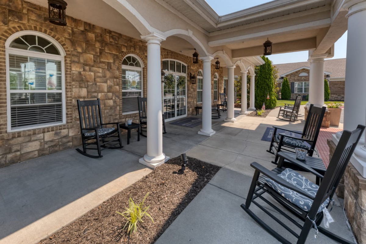 A spacious patio with rocking chairs and columns against a brick wall.
