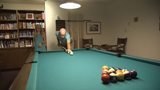 A man prepares to take a shot at the pool table while a woman watches.