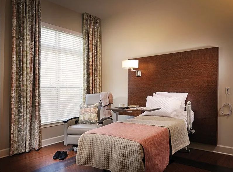 A cozy hospital room with a single bed, chair, and a large window.