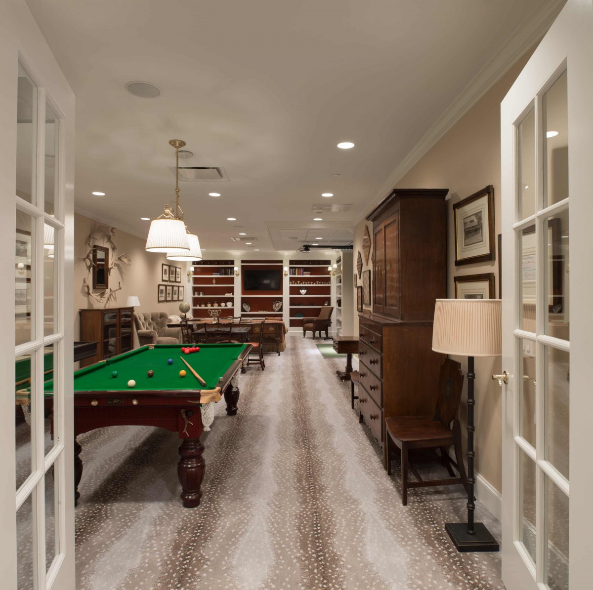 A cozy game room featuring a billiards table and bookshelves, complemented by elegant furnishings and warm lighting.