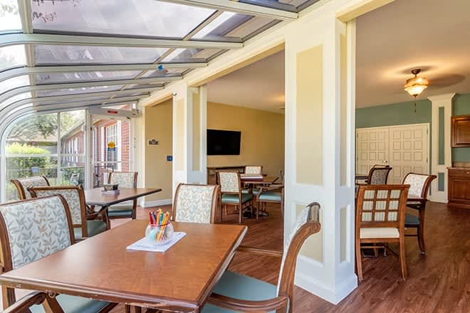 A bright indoor dining area with wooden tables and chairs, featuring a glass ceiling and a television on the wall.