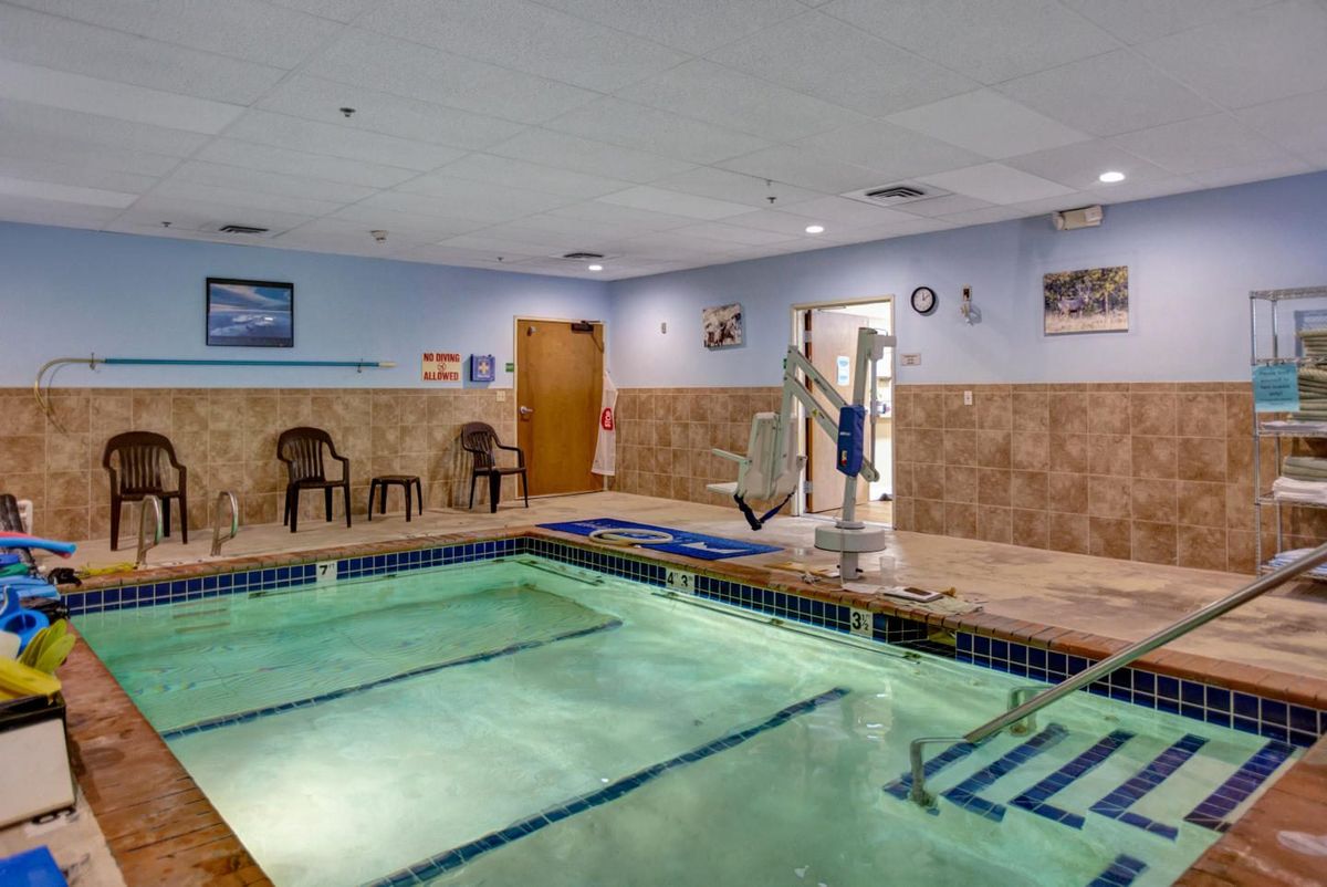 An indoor swimming pool area with chairs and a lift for accessibility.