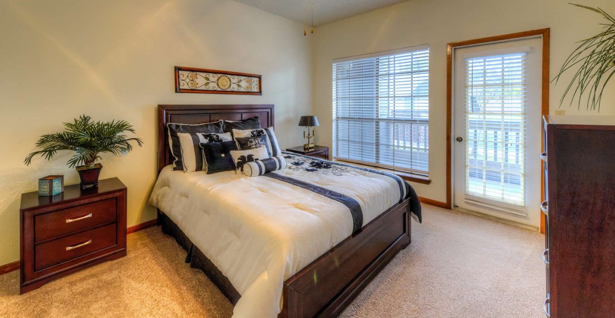 A cozy bedroom with a wooden bed frame, neatly arranged pillows, and a large window allowing natural light to fill the room.