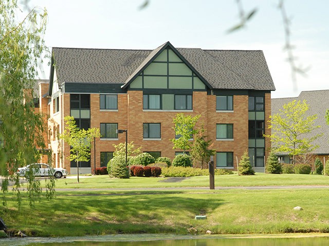 A brick residential building surrounded by trees and greenery.