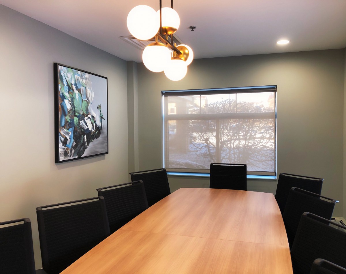 A modern conference room featuring a long meeting table, black chairs, contemporary artwork on the wall, and soft overhead lighting.