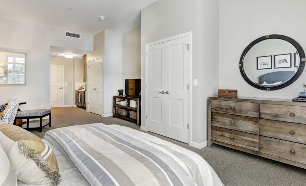 A modern and cozy bedroom with neutral colors, featuring a bed, dresser, and TV.