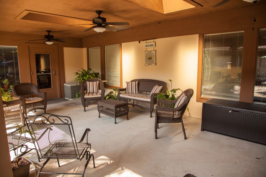 A cozy patio with wicker furniture and ceiling fans, surrounded by plants.