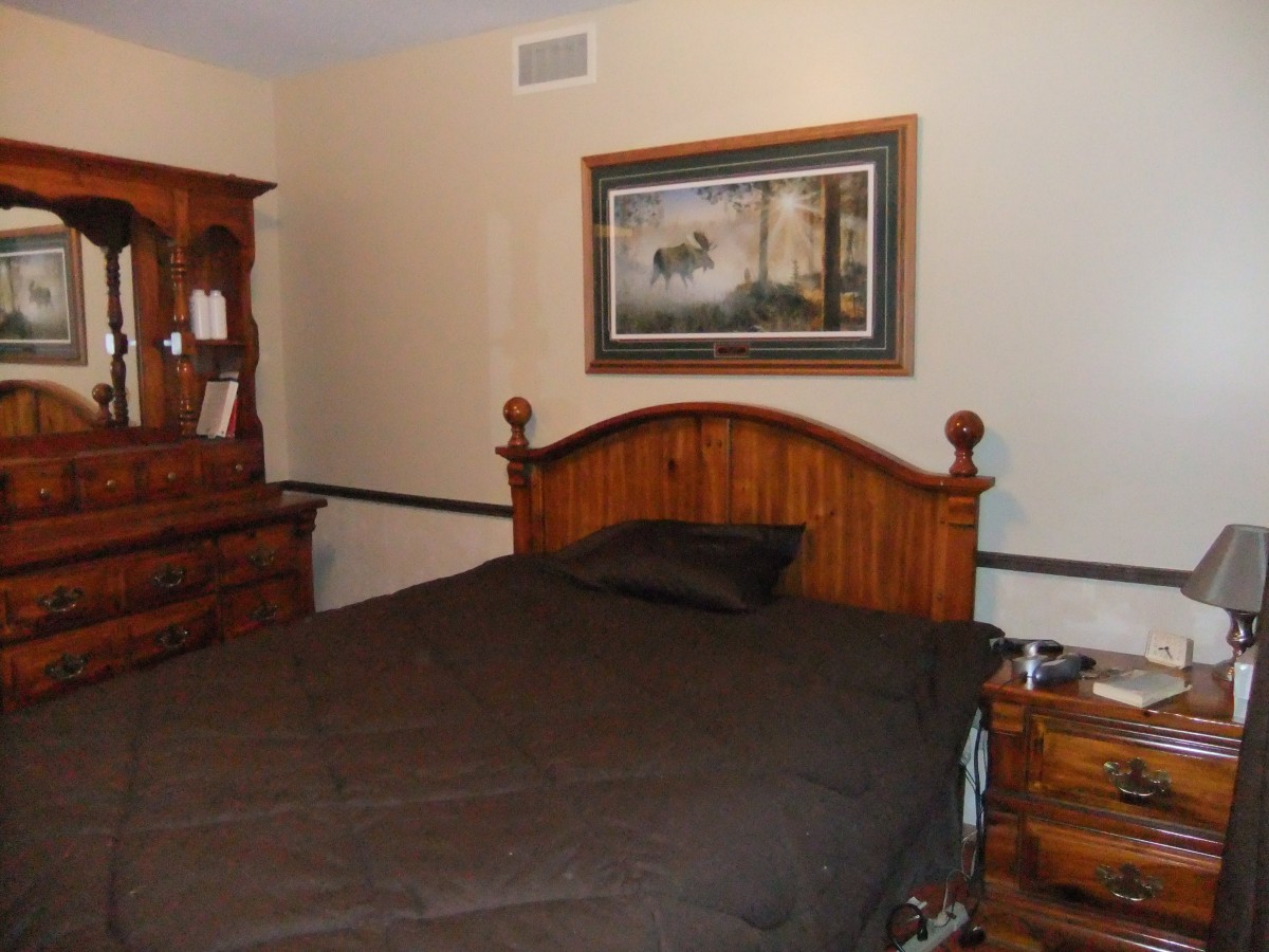 A cozy bedroom featuring a bed with a wooden headboard, a dresser, and a framed painting on the wall.