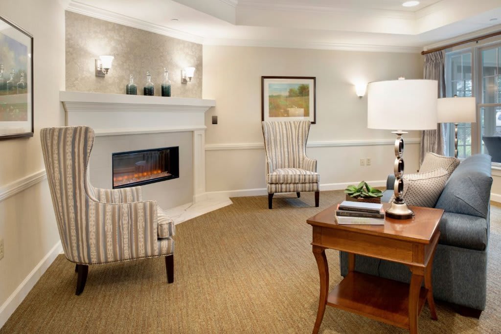 A cozy living room with a fireplace, armchairs, and a table lamp creating a warm atmosphere.
