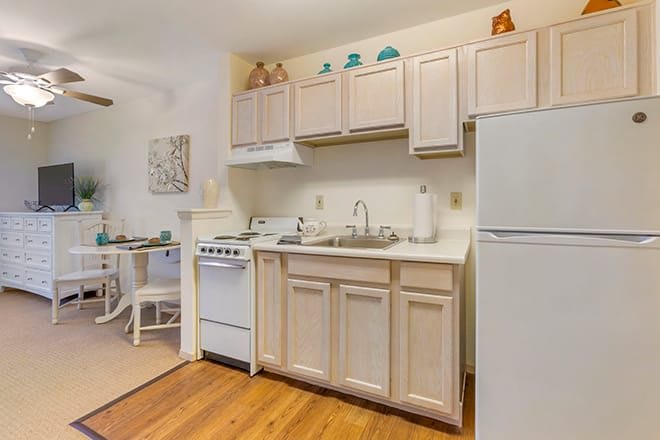 A cozy apartment kitchen with light cabinetry, a stove, refrigerator, and wood flooring.