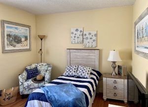 A cozy bedroom features a single bed with striped bedding, an armchair, and beach-themed decorations.