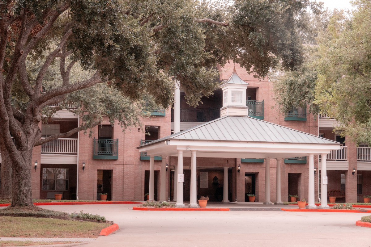 A brick building with a prominent entrance surrounded by trees.