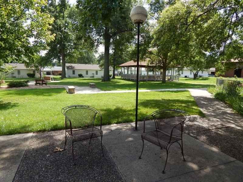 A serene park setting with two metal chairs, a lamp post, and a gazebo in the distance.